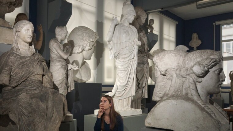 Eine junge Frau betrachtet nachdenklich in den Antikensammlungen eine Sitzstatue der Demeter.
