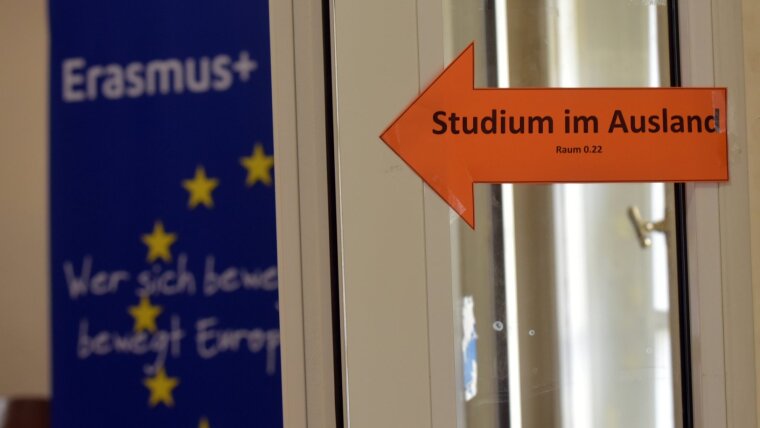 Ein in Signalfarbe gestalteter Pfeil mit der Aufschrift »Studium im Ausland« verweist auf ein Erasmus-Plakat.