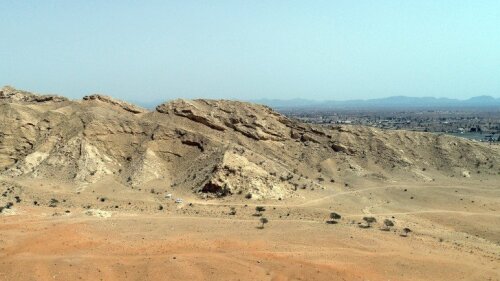 Das Foto zeigt das südliche Ende des Jebel Buhais mit der Fundstelle Buhais Rockshelter im Zentrum des Bildes und das Hajar Gebirge im Hintergrund
