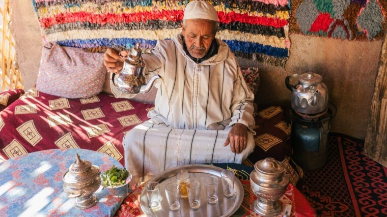 Moroccan man in traditional dress doing ritual preparation of mint tea on outdoor terrace